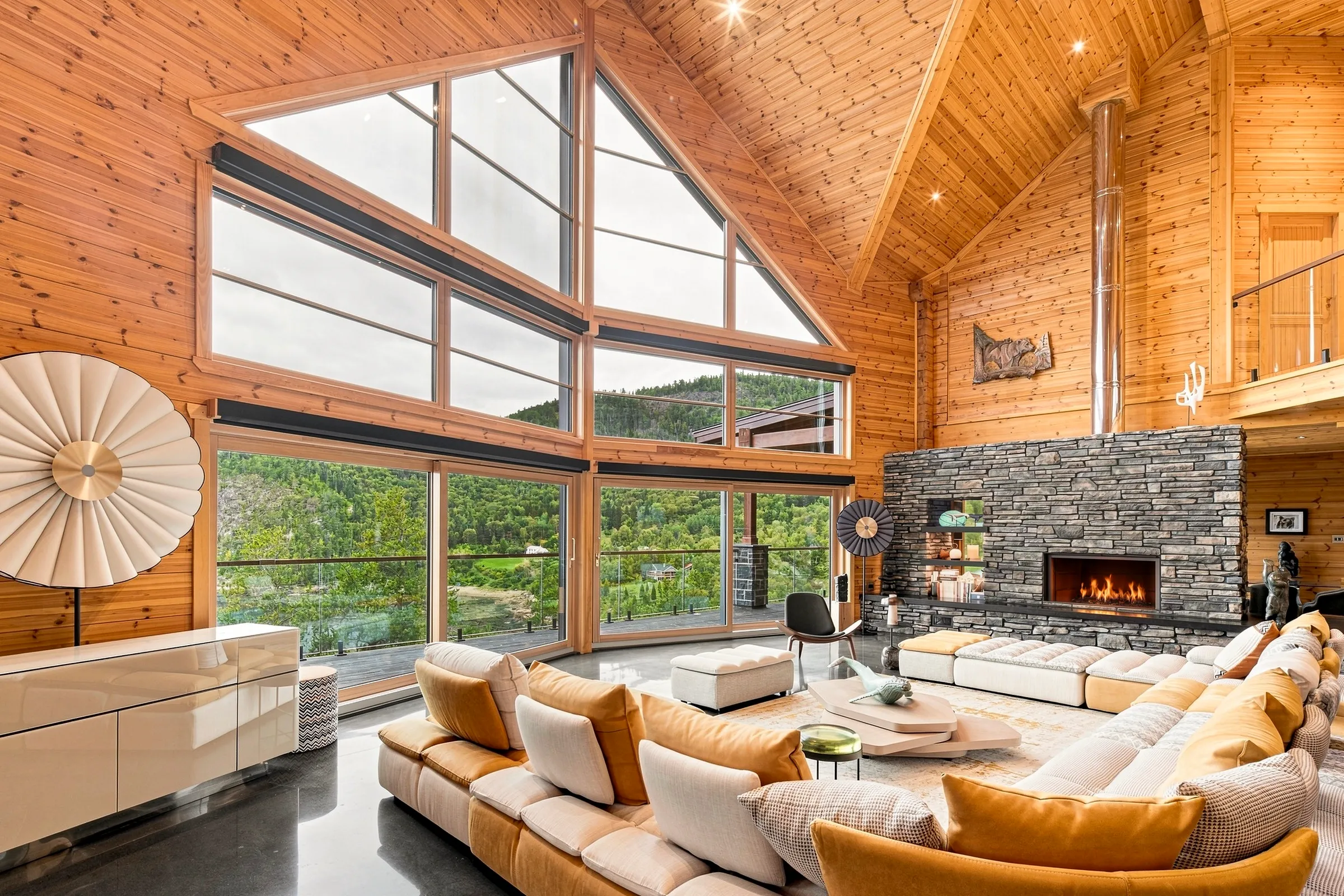 Séjour de chalet en bois rond sous plafond cathédrale, foyer de pierre et baies vitrées sur le fleuve