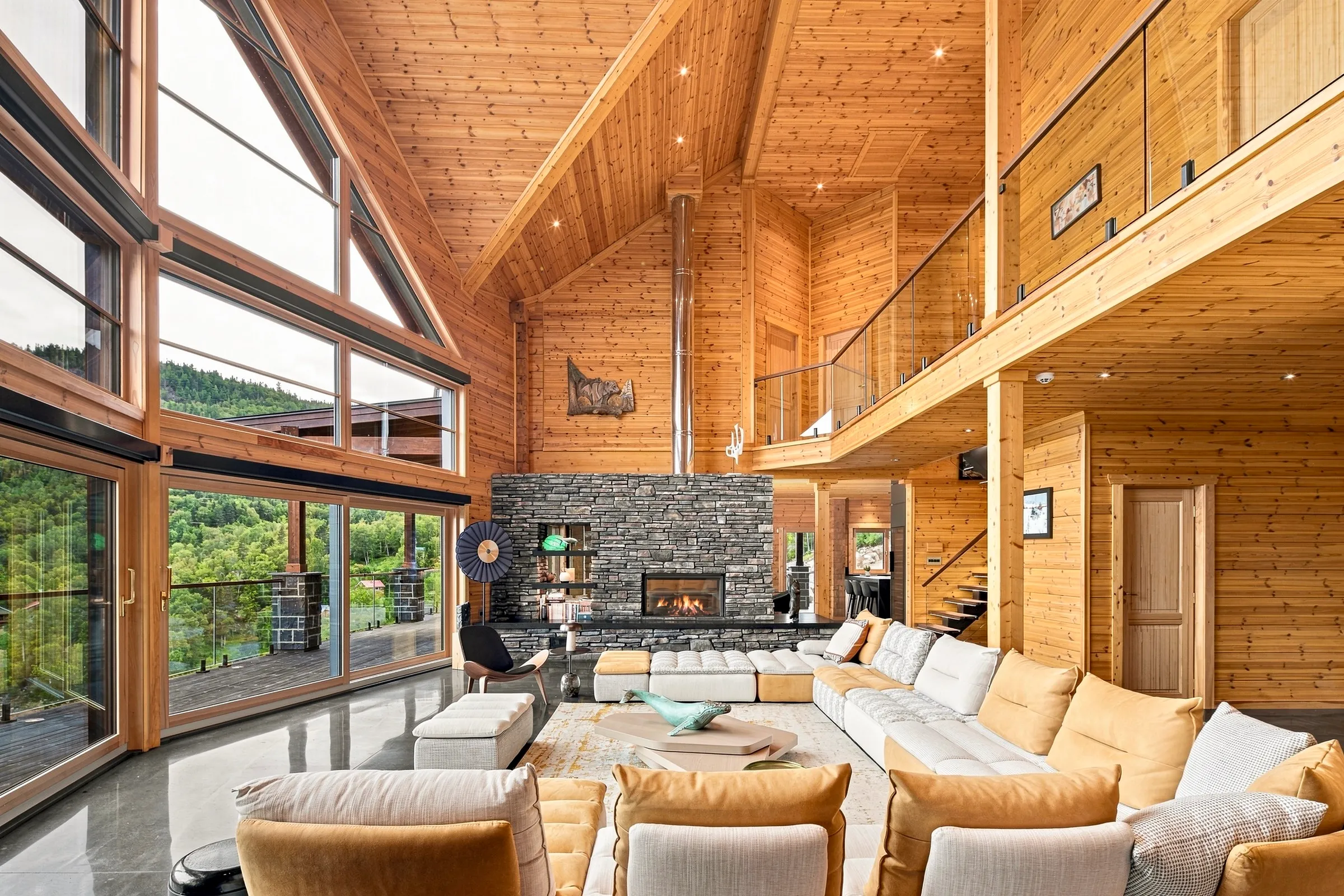 Grand salon de chalet en bois, mezzanine et fenêtres en pignon ouvertes sur les montagnes