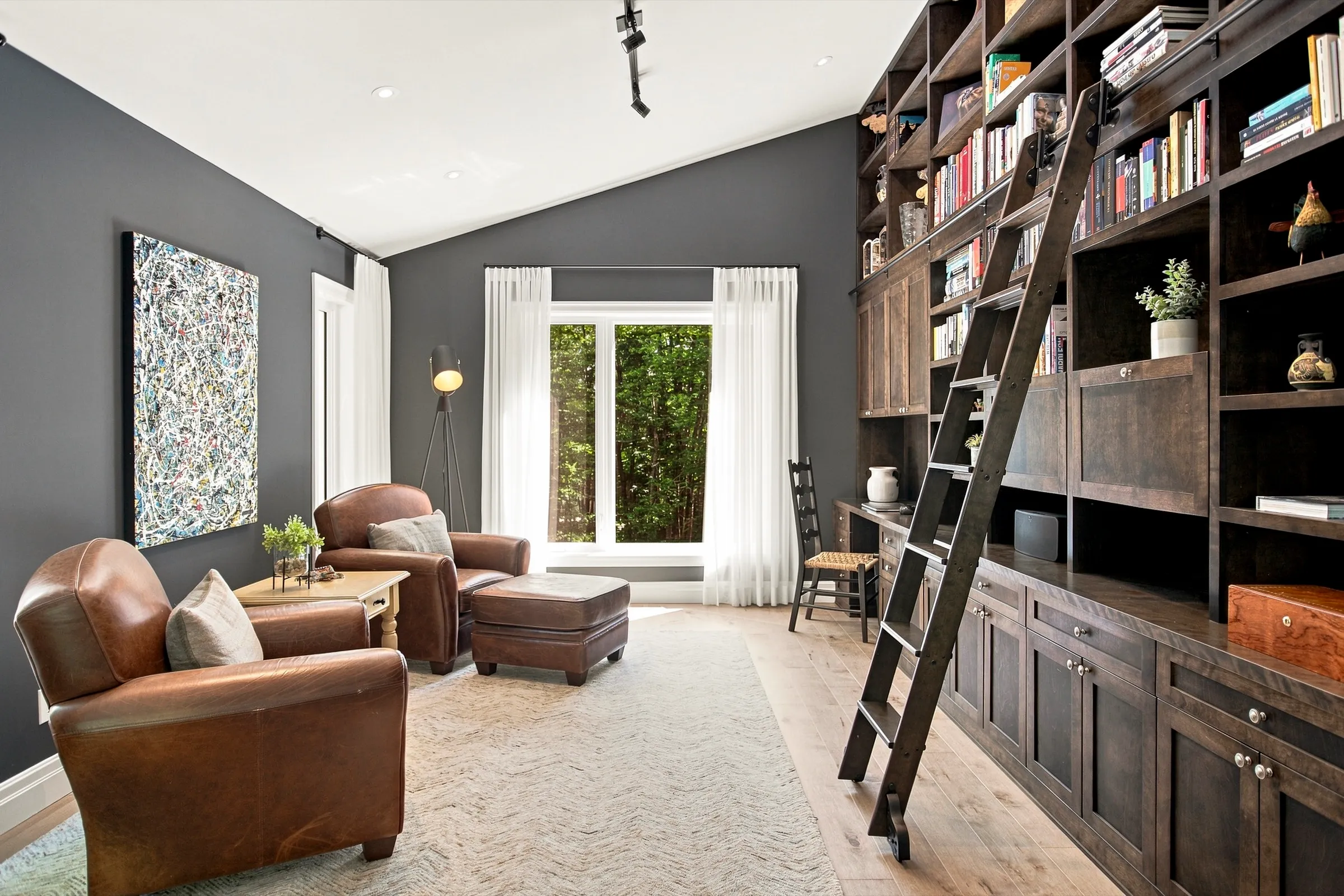 Bibliothèque murale de bois sombre avec échelle coulissante, fauteuils de cuir devant une fenêtre