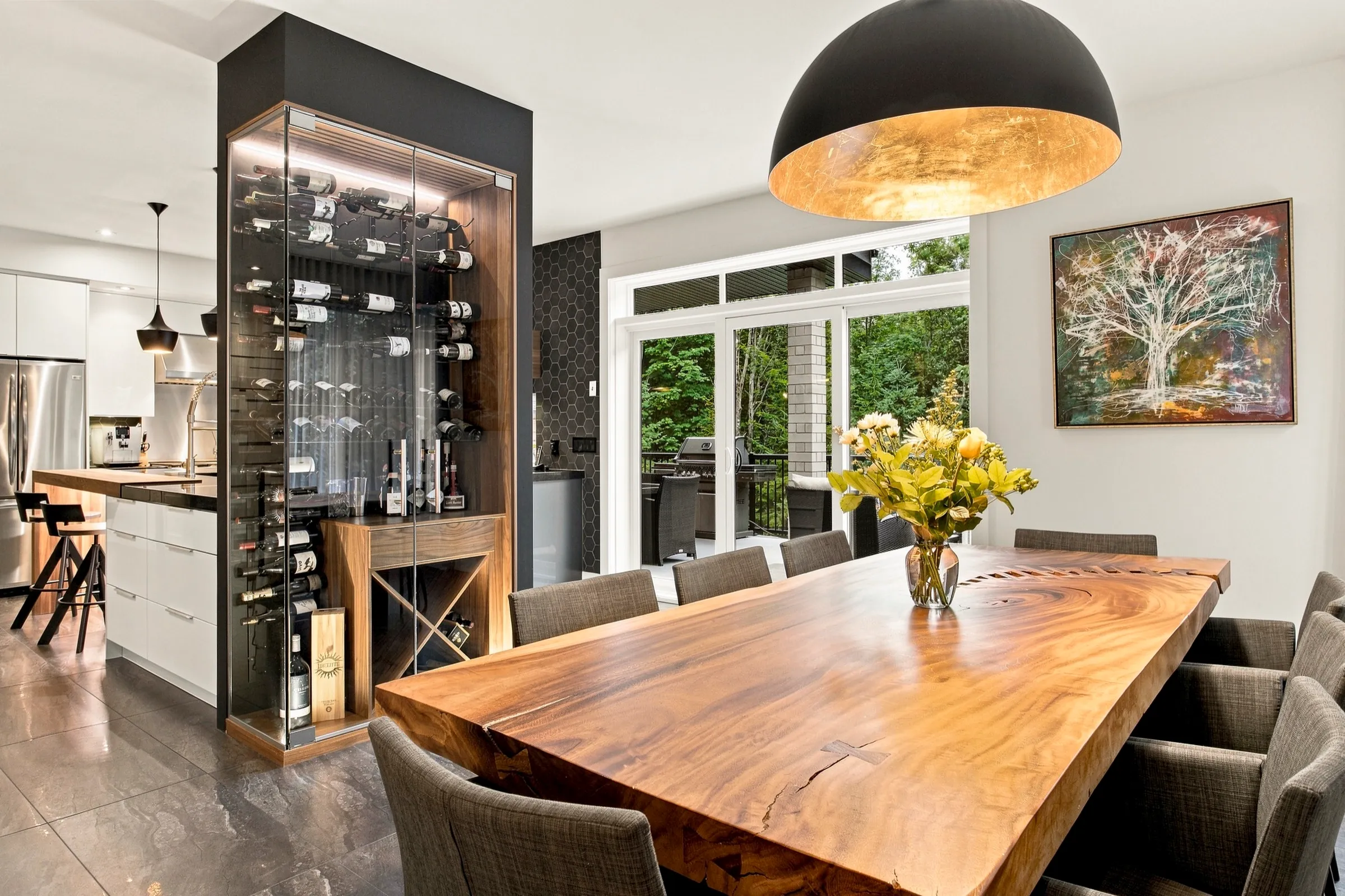 Salle à manger avec longue table de bois massif, suspension noire et cellier vitré en arrière-plan