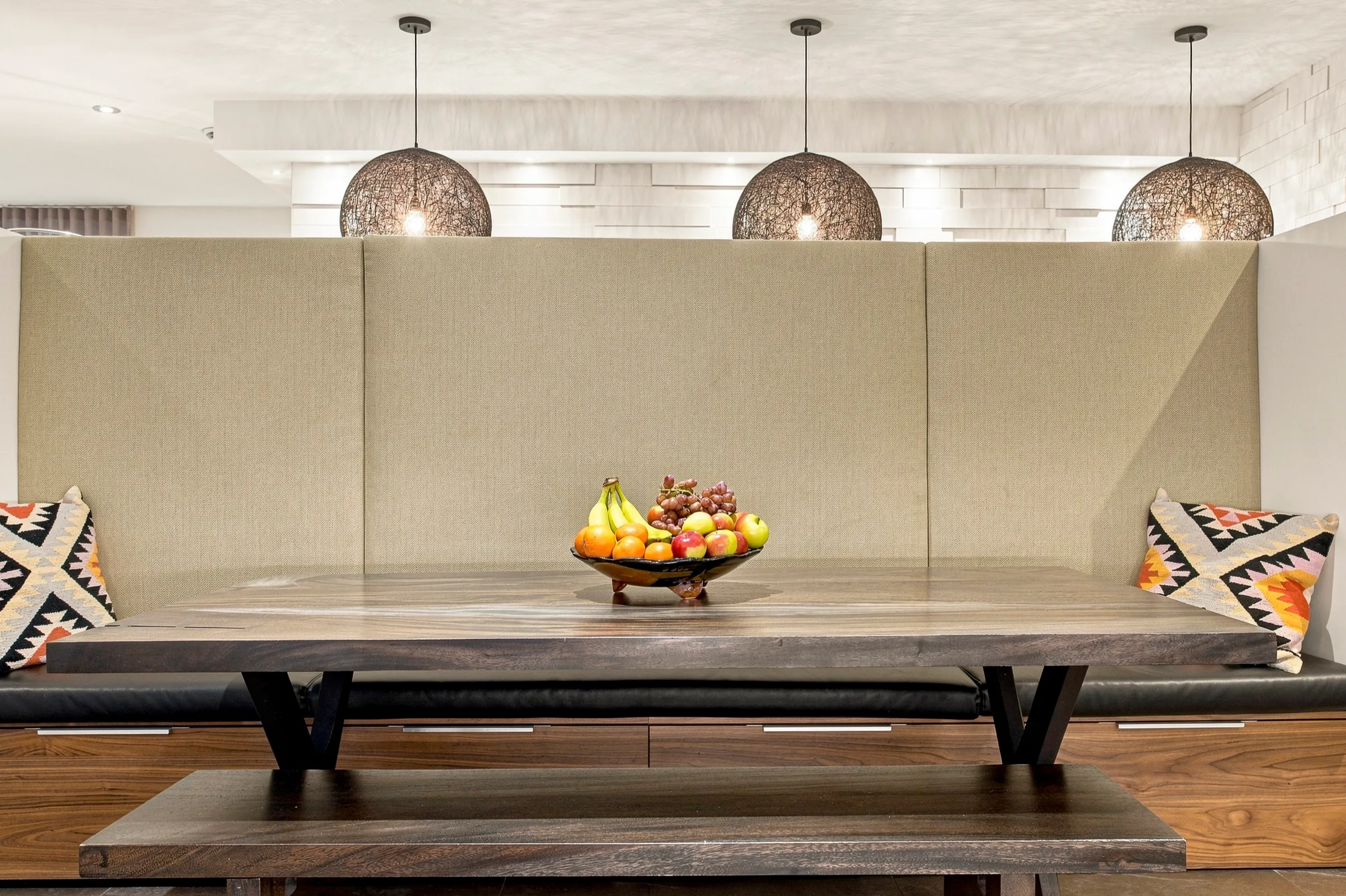 Salle à manger design, banquette adossée à une cloison claire sous trois suspensions de verre