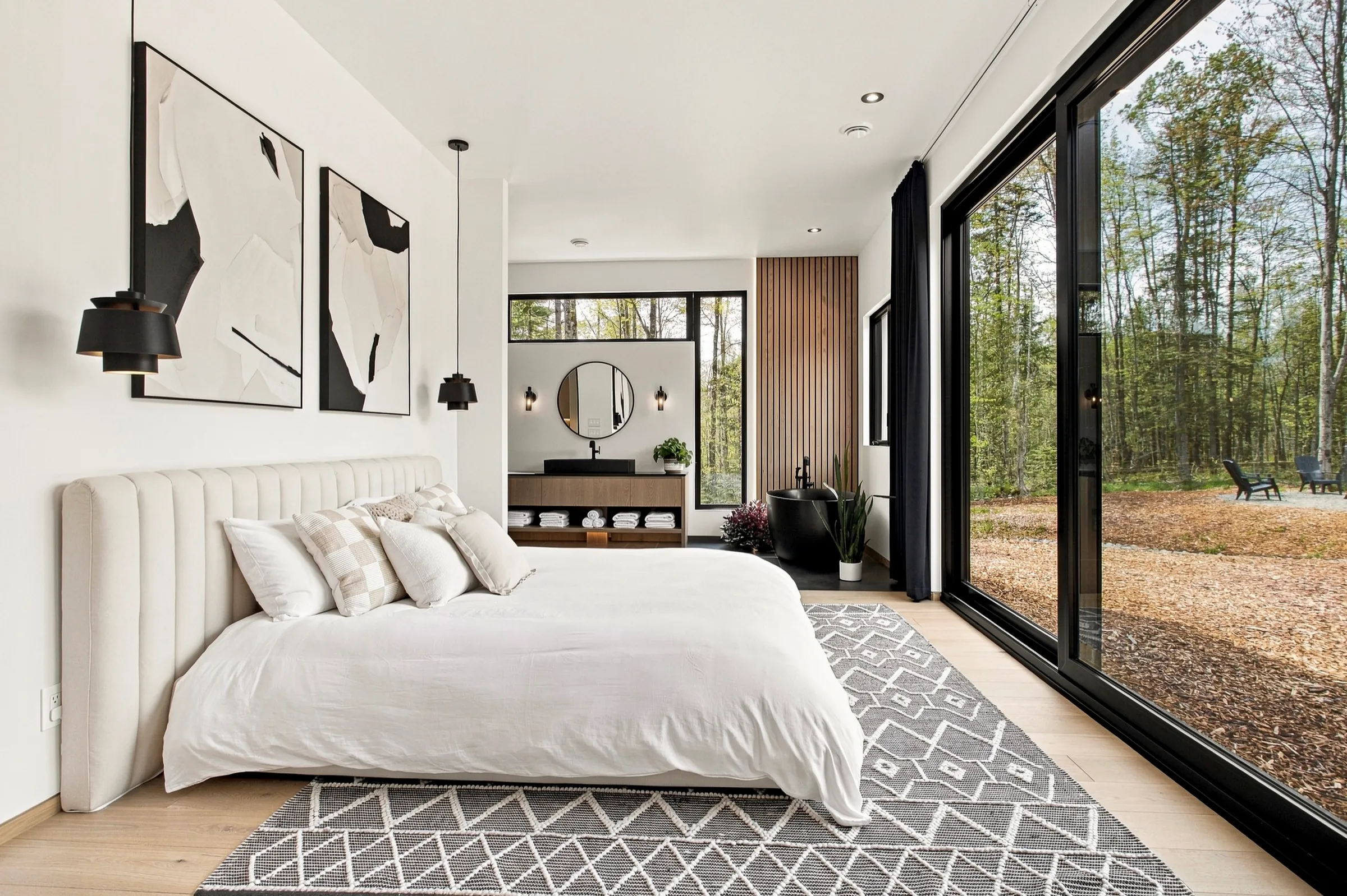Chambre aux murs blancs ouverte de plain-pied sur un boisé par une baie vitrée pleine hauteur