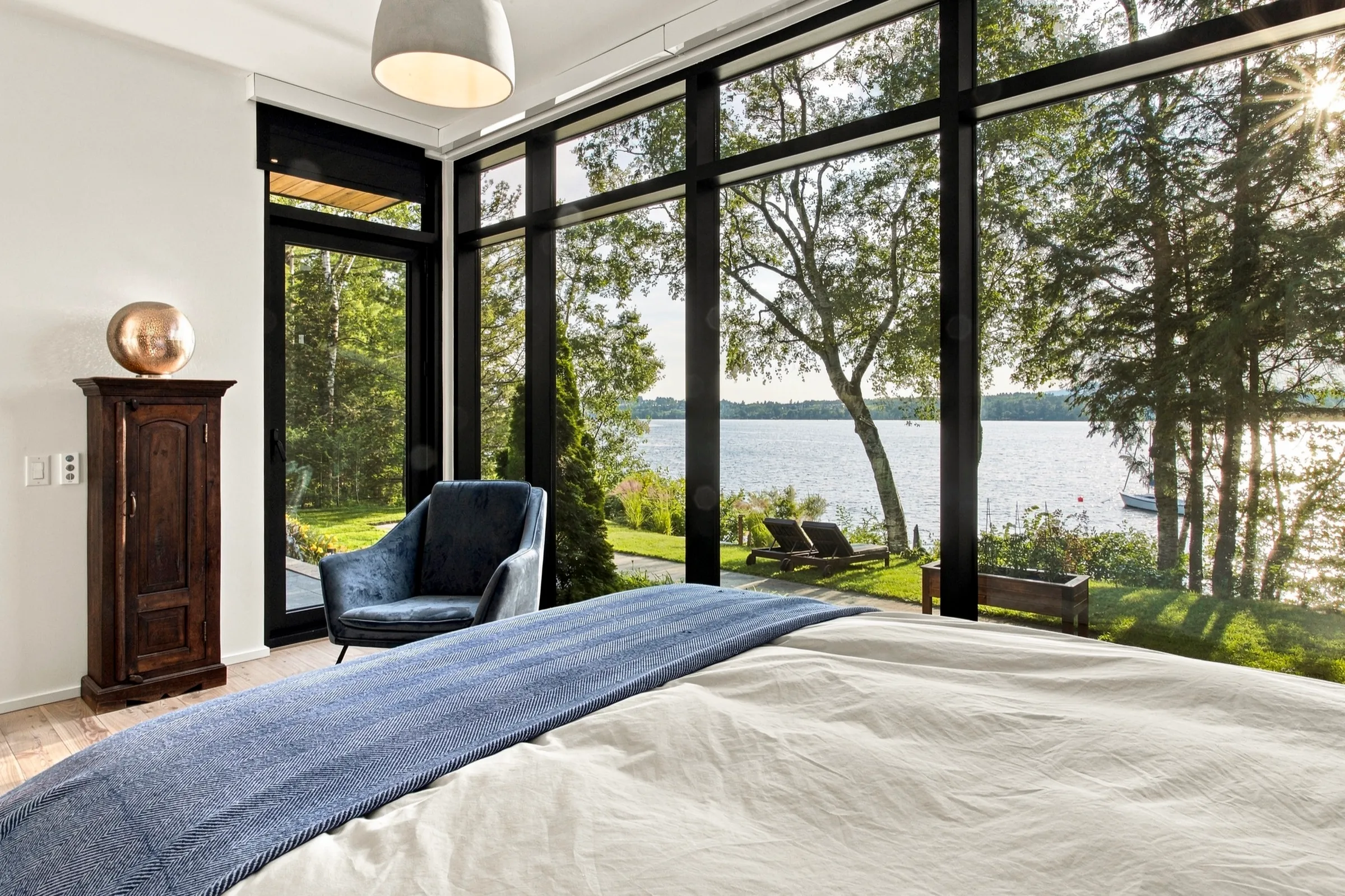 Chambre bordée de fenêtres du sol au plafond, fauteuil bleu et vue sur le lac