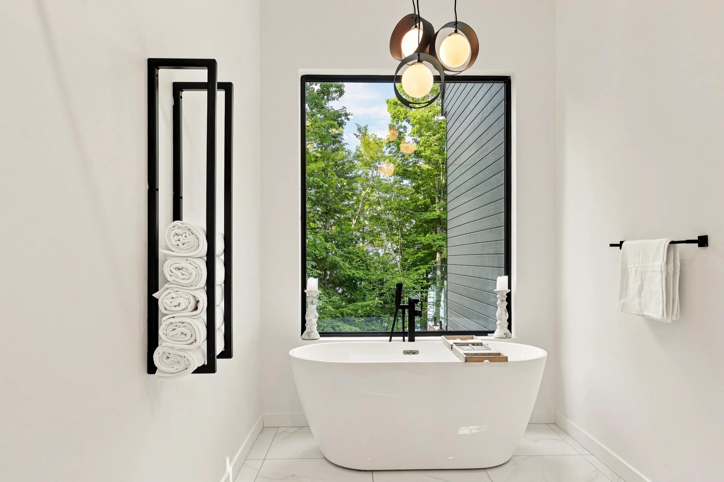 Salle de bain blanche épurée, baignoire autoportante devant une fenêtre ouverte sur les arbres