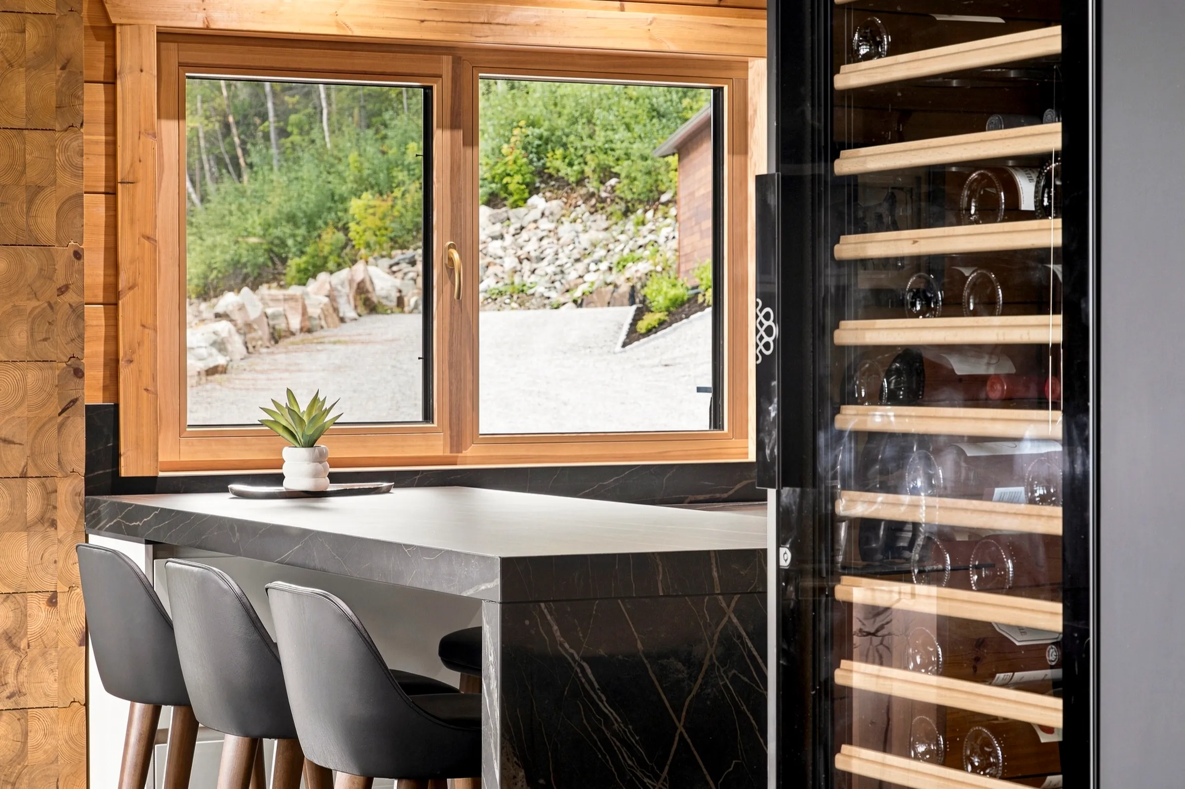 Coin repas devant une cave à vin vitrée toute hauteur, comptoir de pierre sombre