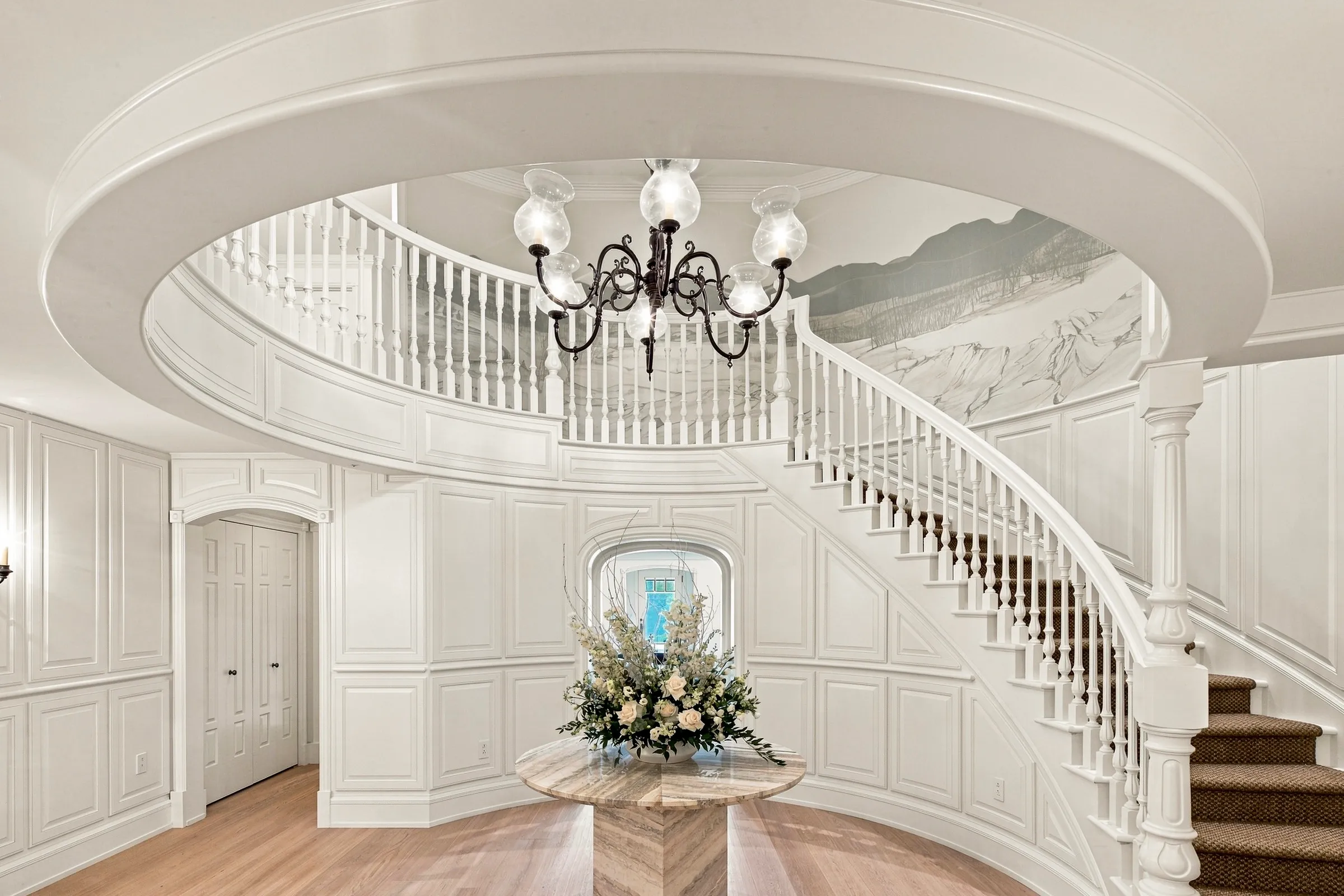 Hall de réception classique, escalier courbe à balustres blancs sous un lustre à pampilles