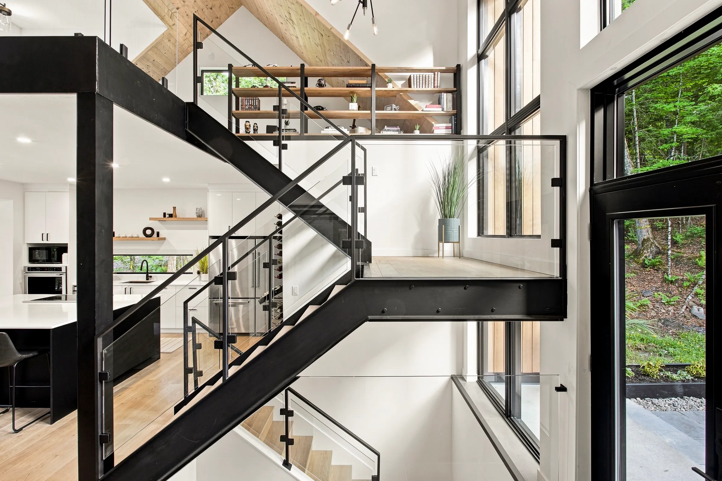 Escalier d’acier noir suspendu dans un volume vitré sur deux étages, mezzanine à garde-corps de verre