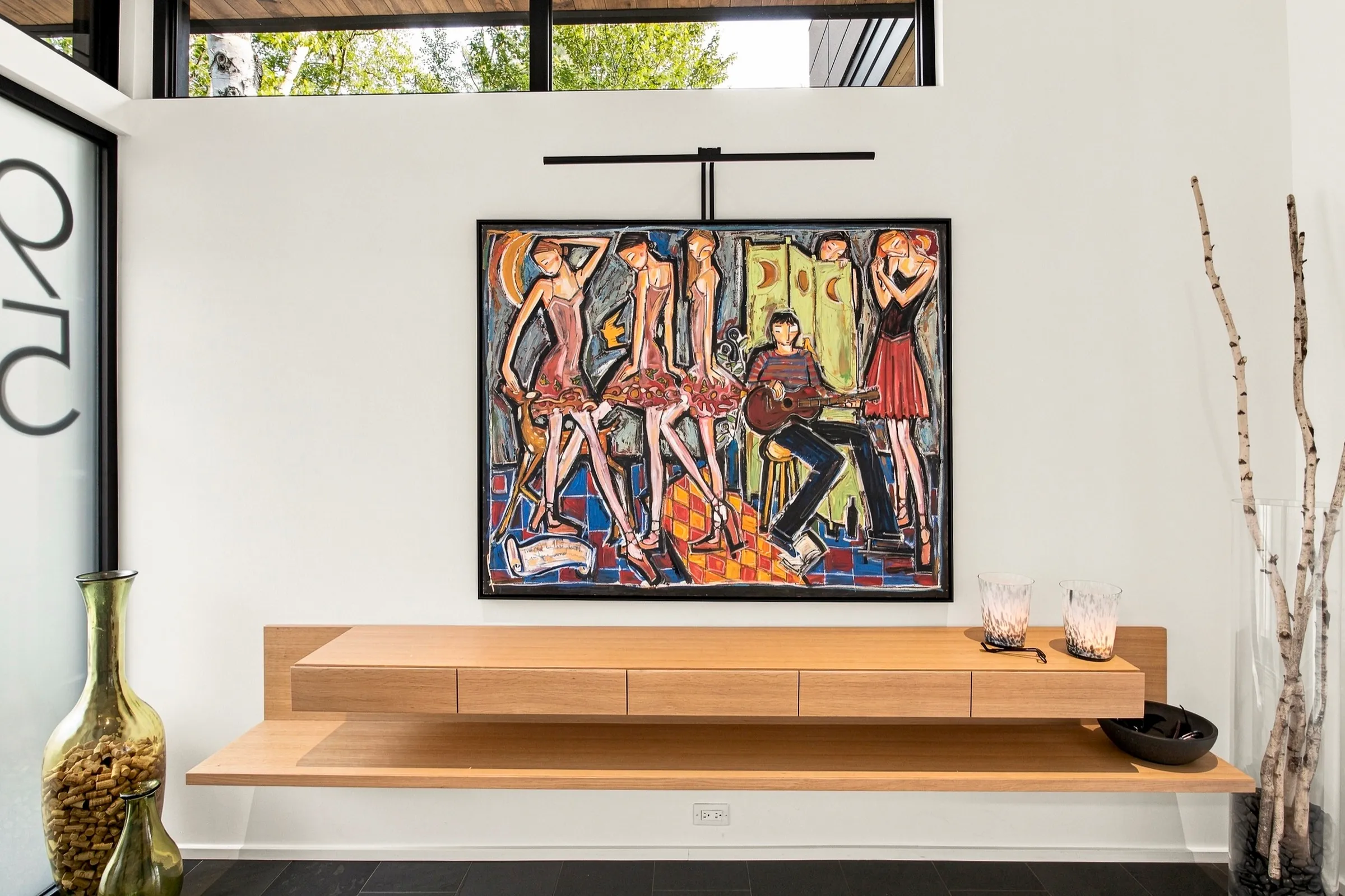 Banc de bois massif sous une grande toile figurative, mur clair et objets de céramique