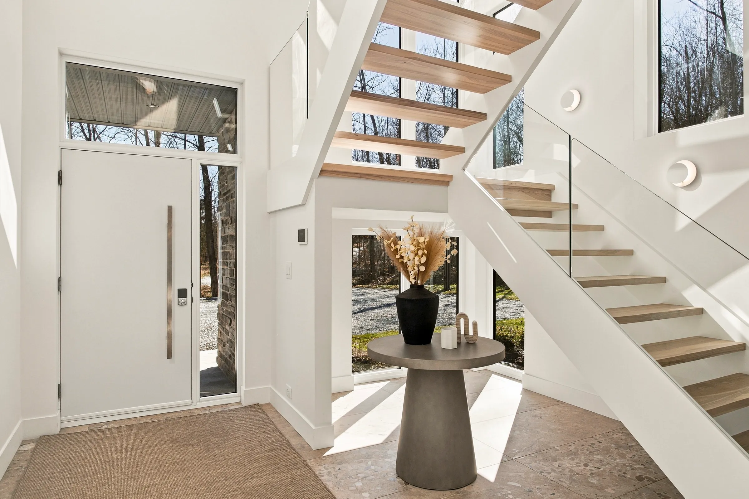 Hall d’entrée vitré, escalier de bois clair à limon blanc et console ronde
