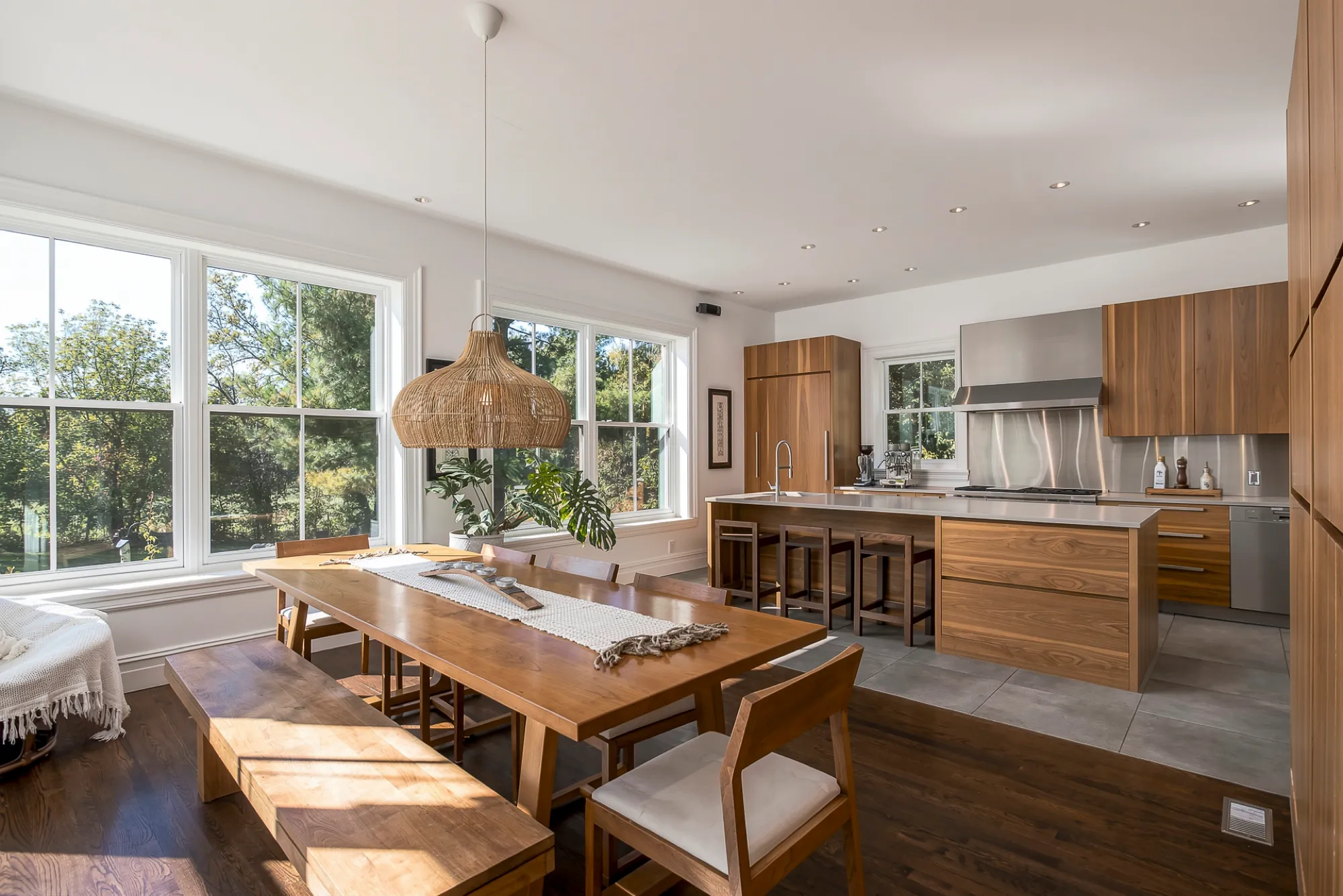 Cuisine de noyer ouverte sur une grande table de bois, baies vitrées sur les arbres